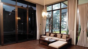 A spacious living room with a large window, a sofa, a coffee table, and a chandelier. - Acasa Cottage by Samsara (Ciawi)