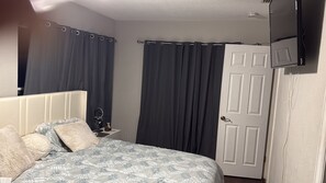 A bedroom with a bed, curtains, a door, and a bedside table. - Cozy accommodations right near everything (Clearwater)