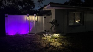 A house with a purple-lit fence, a cactus, and a lit pathway. - Cozy accommodation very close to everything (Clearwater)