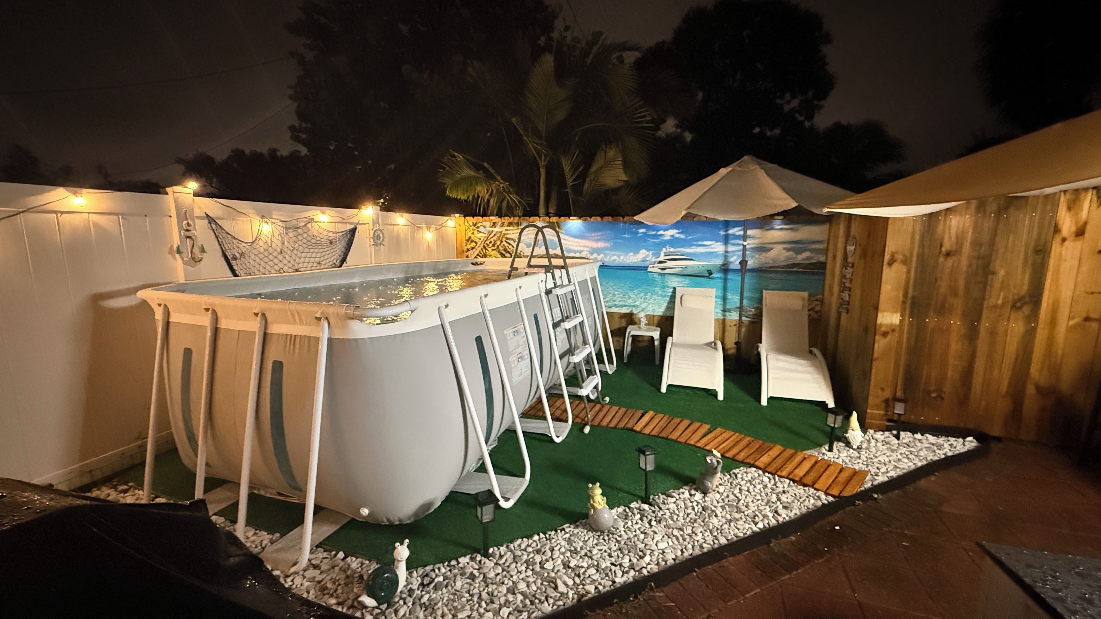 A pool with a ladder, surrounded by chairs and a mural of a beach scene.