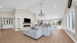 Un salón espacioso con chimenea, un sofá grande, una zona de comedor y una cocina con armarios blancos.