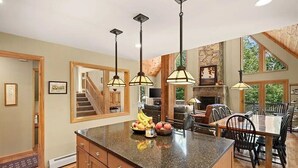 A spacious kitchen with a large island, pendant lights, and a stone fireplace.