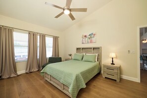 A bedroom with a bed, a nightstand, a ceiling fan, and a window with curtains.
