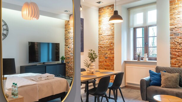 Una habitación de hotel moderna con una cama, un televisor, un comedor con mesa y sillas, un sofá y un espejo grande.