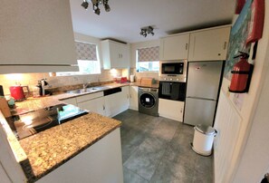 A compact kitchen with white cabinets, a granite countertop, a microwave, an oven, and a washing machine.