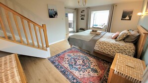 Quarto com cama, escada de madeira, tapete estampado e vista para o exterior.
