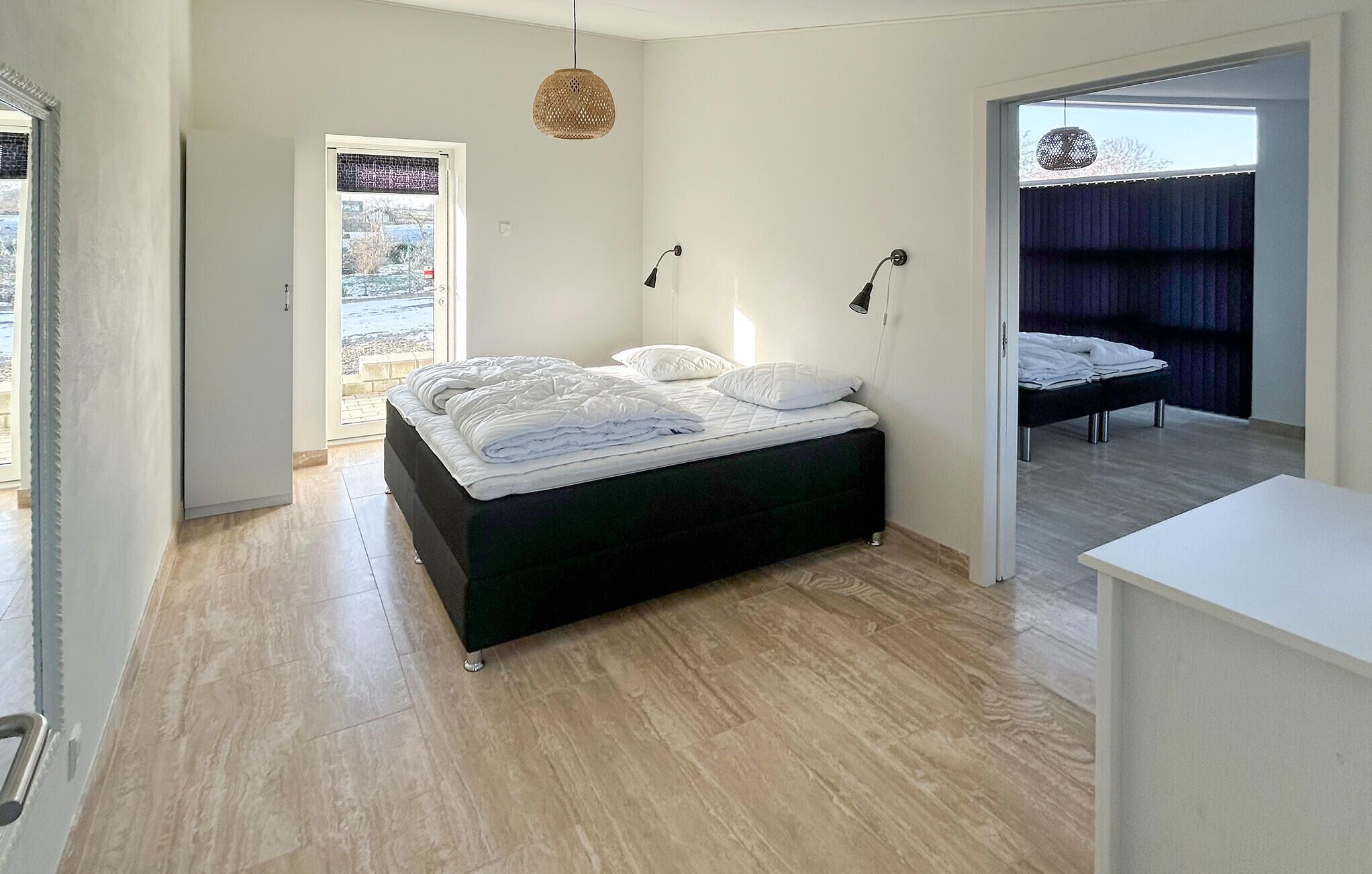 A modern bedroom with a bed, bedside lamps, a view through a door, and a small desk area.