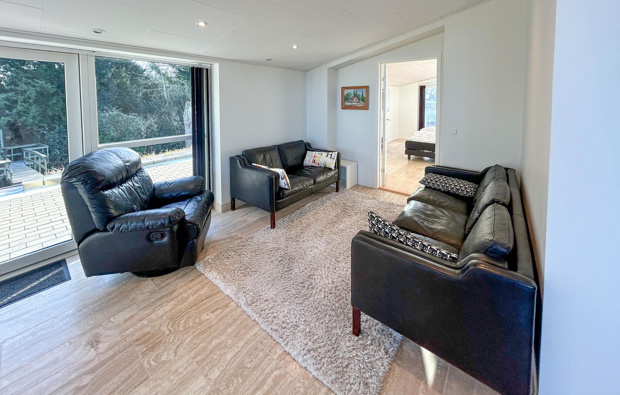 A modern living room with leather sofas, a fluffy rug, and large windows offering a view of the outdoors.