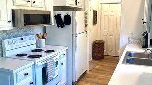 Una cucina moderna con mobili bianchi, un forno a microonde in acciaio inossidabile, un frigorifero bianco e un piano cottura.