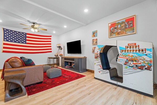 Un salon avec un grand drapeau américain, un téléviseur, une console de jeux et un tapis rouge.