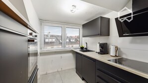 A modern kitchen with black cabinets, a white countertop, and a window with blinds.