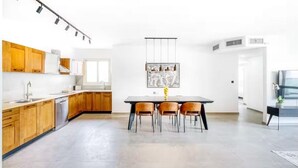 A modern kitchen with wooden cabinets, a dining table with four chairs, and a hanging light fixture.