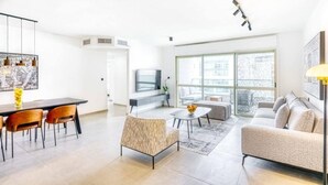 A modern living room with a sofa, a dining table with chairs, a TV, and large windows.