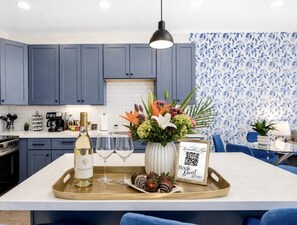 A modern kitchen with blue cabinets, a central island with a tray of food and drinks, and a QR code sign. - Luxury 3BR Townhome: Pool- King Beds- Garage- Close to Airport (Phoenix)