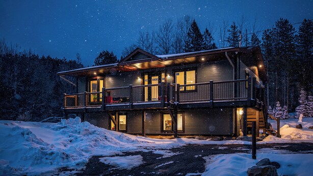 A two-story lodge with a balcony, wooden exterior, and a lit interior. - Hot Tub Lakeside Cottage – 30 Min from Mont Tremblant (Labelle)
