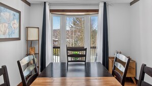 A dining area with a wooden table and chairs, a bench, a lamp, and a view through a large window. - Hot Tub Lakeside Cottage – 30 Min from Mont Tremblant (Labelle)