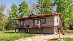 A two-story cabin with a balcony, a covered porch, and a gravel driveway. - Hot Tub Lakeside Cottage – 30 Min from Mont Tremblant (Labelle)