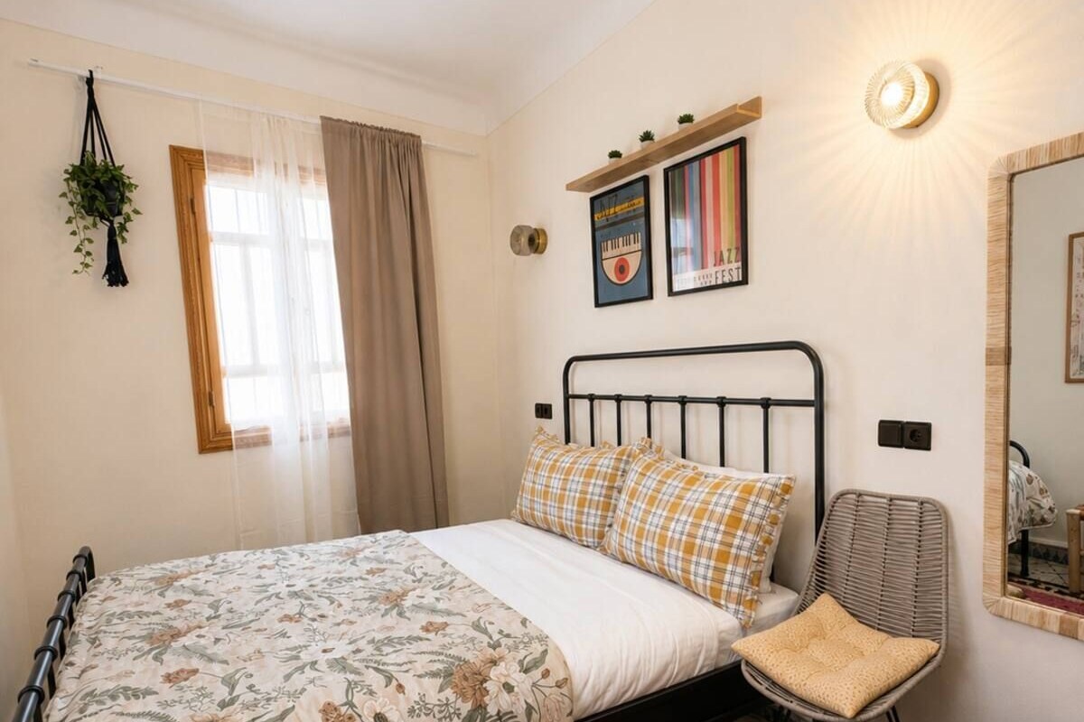 A bedroom with a bed, a chair, a rug, a hanging plant, and a wall-mounted shelf with decorative items.