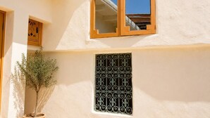 Un edificio con ventana de marco de madera y reja metálica, una planta en maceta y un pequeño mueble de madera.