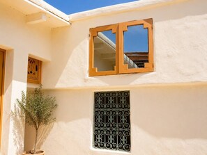 A building with a window with a wooden frame and a metal grill, a potted plant, and a small wooden cabinet. - Dana Social Living (Marrakech)