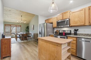 A modern kitchen with wooden cabinets, stainless steel appliances, and a dining area with a table and chairs. - The Beechline~Walk to Slopes~Mtn & Slope Views~Private Club Access~Sleeps 12 (Beech Mountain)