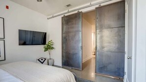 Ein Schlafzimmer mit Bett, einer Schiebetür, einem Blumentopf und einem Wandfernseher.