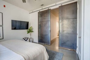 Un dormitorio con cama, una puerta corredera, una planta en maceta y un televisor montado.