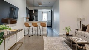 Eine moderne Küche mit Barhocker, ein Essbereich mit einer Couch und ein Wohnzimmer mit Couchtisch.