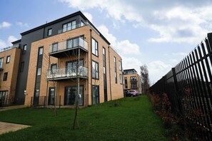 A modern apartment building with multiple balconies, a fenced courtyard, and a clear sky. - 2BR Apartment Near Outlet and Station with Lift (Ashford)