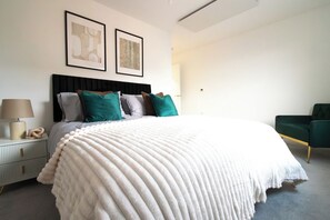 A modern bedroom with a large bed, a bedside table with a lamp, and a green armchair. - 2BR Apartment Near Outlet and Station with Lift (Ashford)