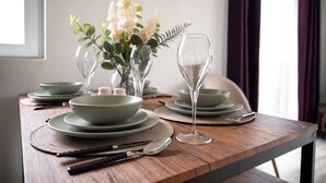 Mesa de jantar posta com pratos, tigelas e uma taça de vinho verdes, acompanhada por um vaso de flores e um garfo.