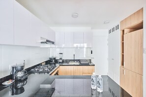 A modern kitchen with white cabinets, a black countertop, and a wooden cabinet on the right. - Geko| Cool 1BR w/ Balcony in Barranco (Barranco)