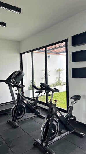 A gym with two stationary bikes, large windows, and a view of a garden. - Geko| Cool 1BR w/ Balcony in Barranco (Barranco)