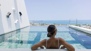 Eine Frau entspannt sich in einem klaren Pool mit Blick auf das Meer und die Stadtlandschaft.