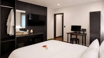 Habitación de hotel con cama, escritorio con computadora, televisor y armario.