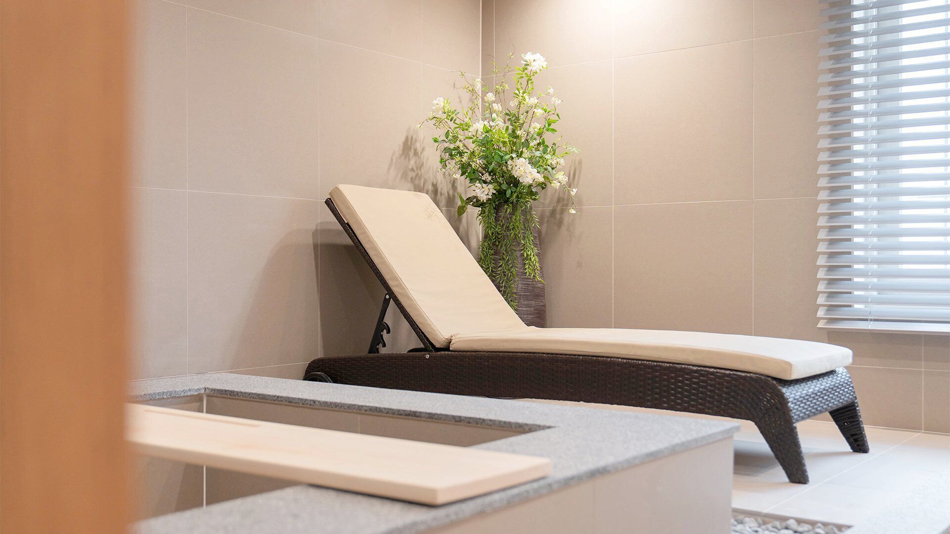 Um quarto de spa com uma cadeira reclinável, uma mesinha e um vaso de planta.