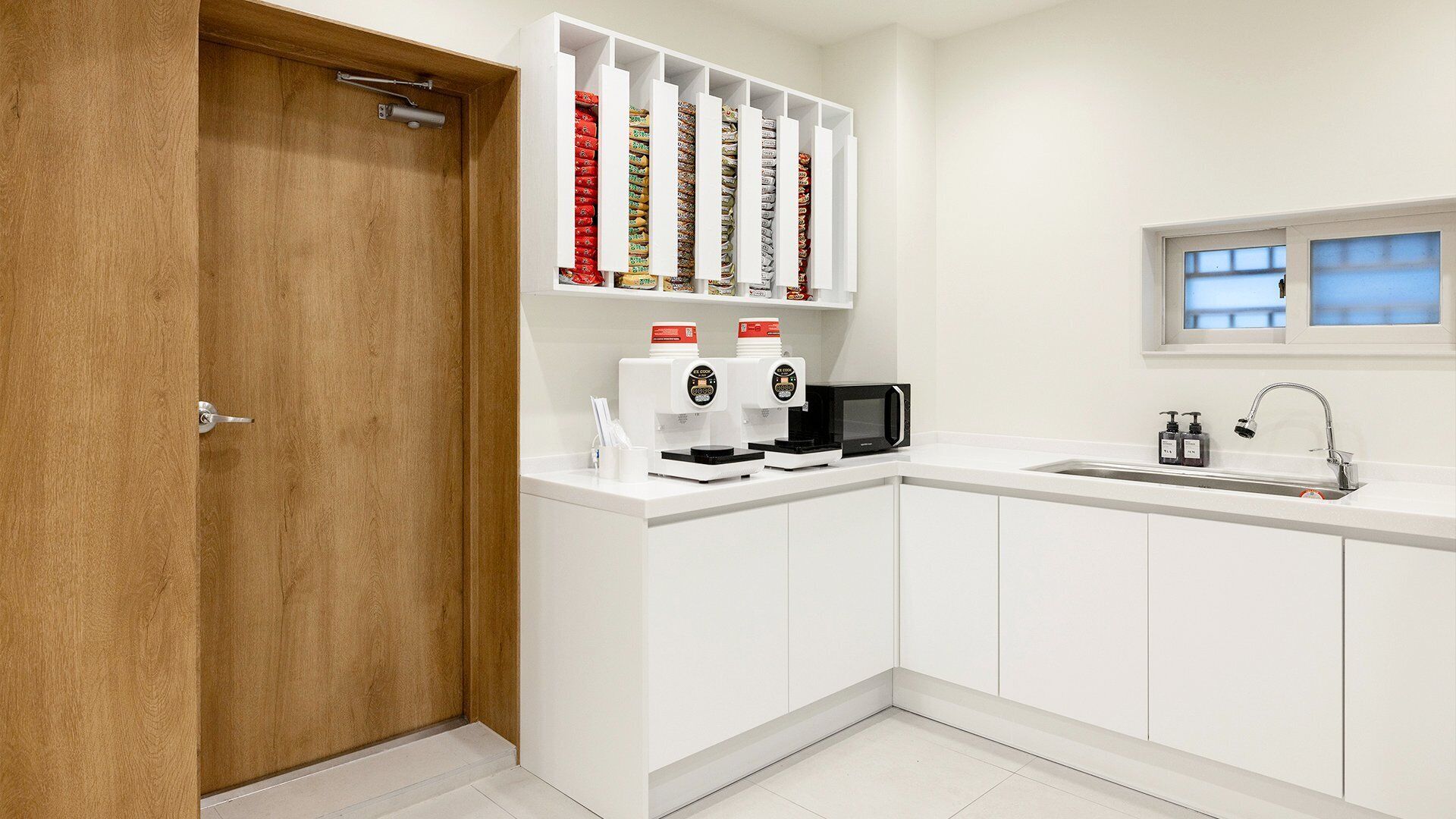 Una cocina moderna con armarios blancos, microondas integrado, cafetera y ventana sobre el fregadero.