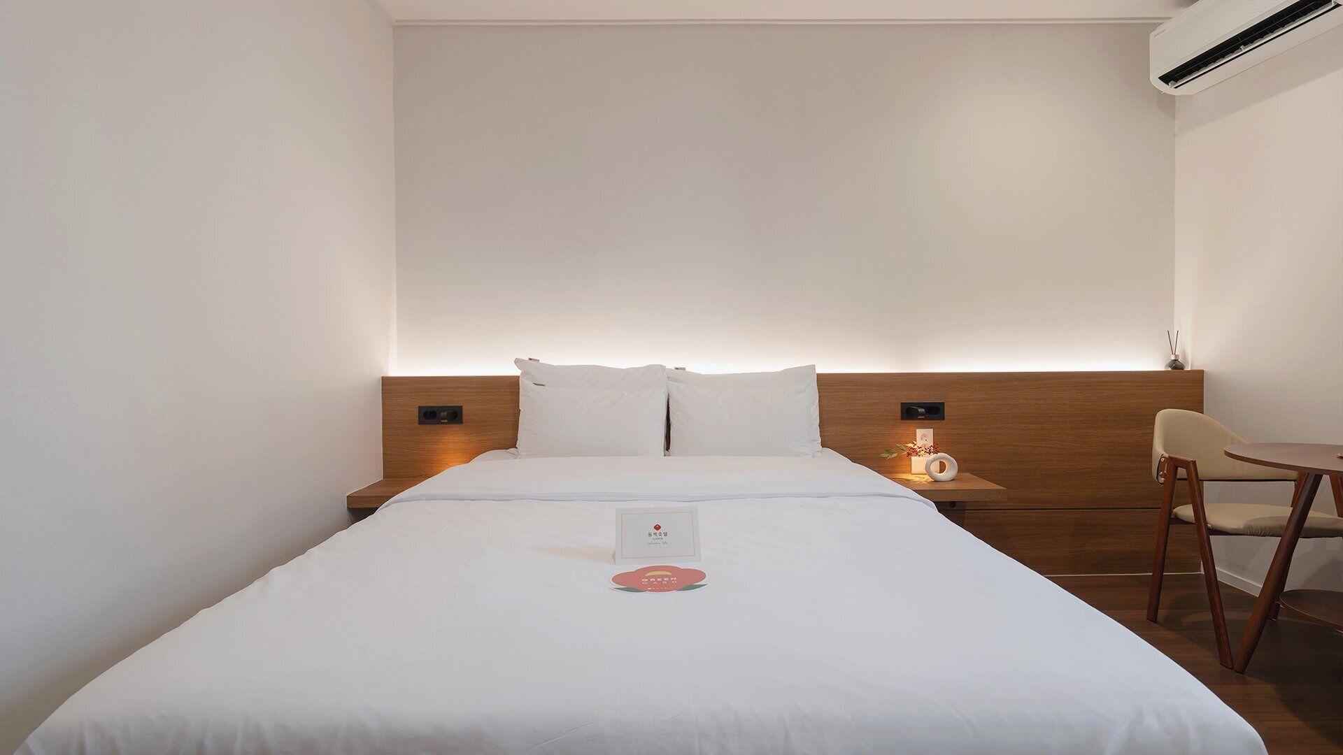 A hotel room with a bed, bedside tables, a chair, and an air conditioning unit.