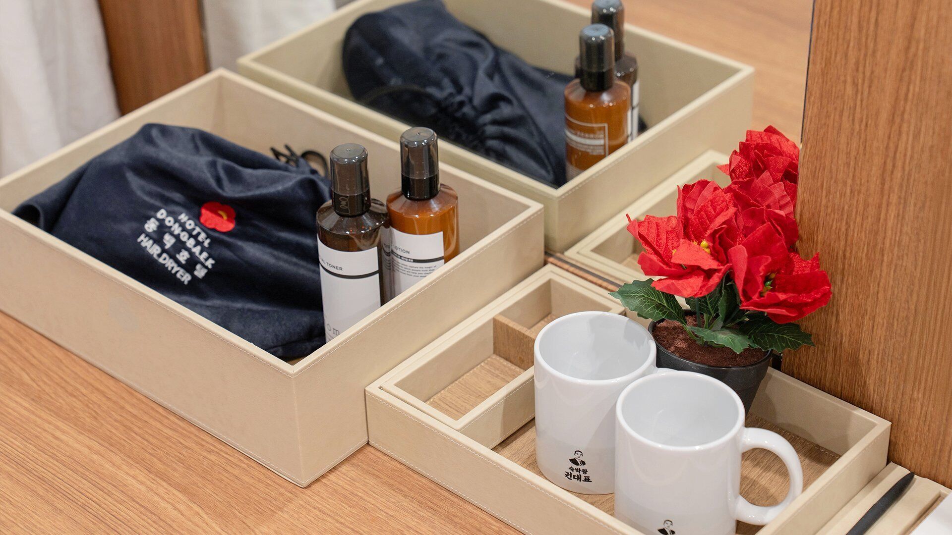 Un cajón ordenado con una camisa azul oscuro, dos botellas y una flor roja.