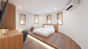 A modern hotel room with a curved wooden floor, a bed with white linens, a desk with a chair, and a TV mounted on the wall. - From H Dongbaek Hotel by kwon Cheonan Seongjeong (Cheonan)
