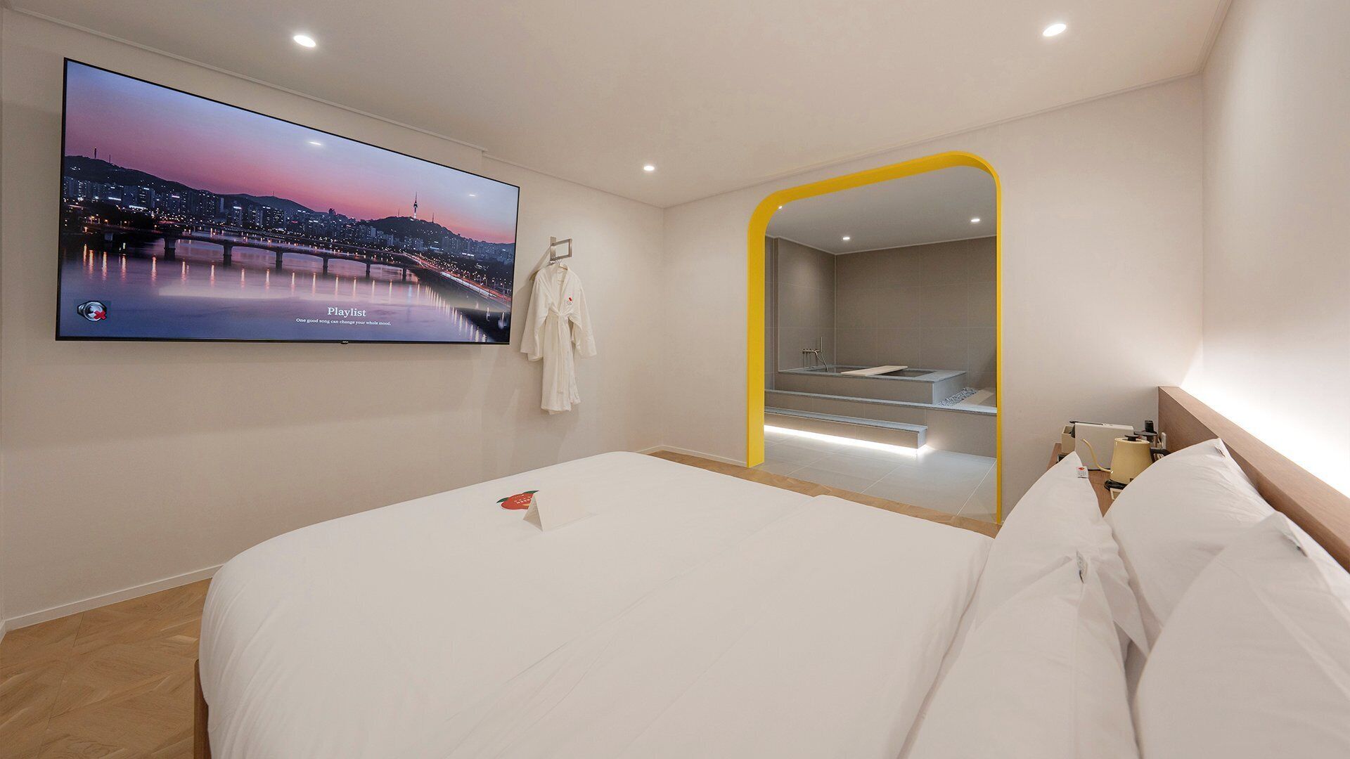 Una habitación de hotel moderna con una cama grande, un televisor montado en la pared, un baño con espejo y una escalera que lleva a un nivel superior.