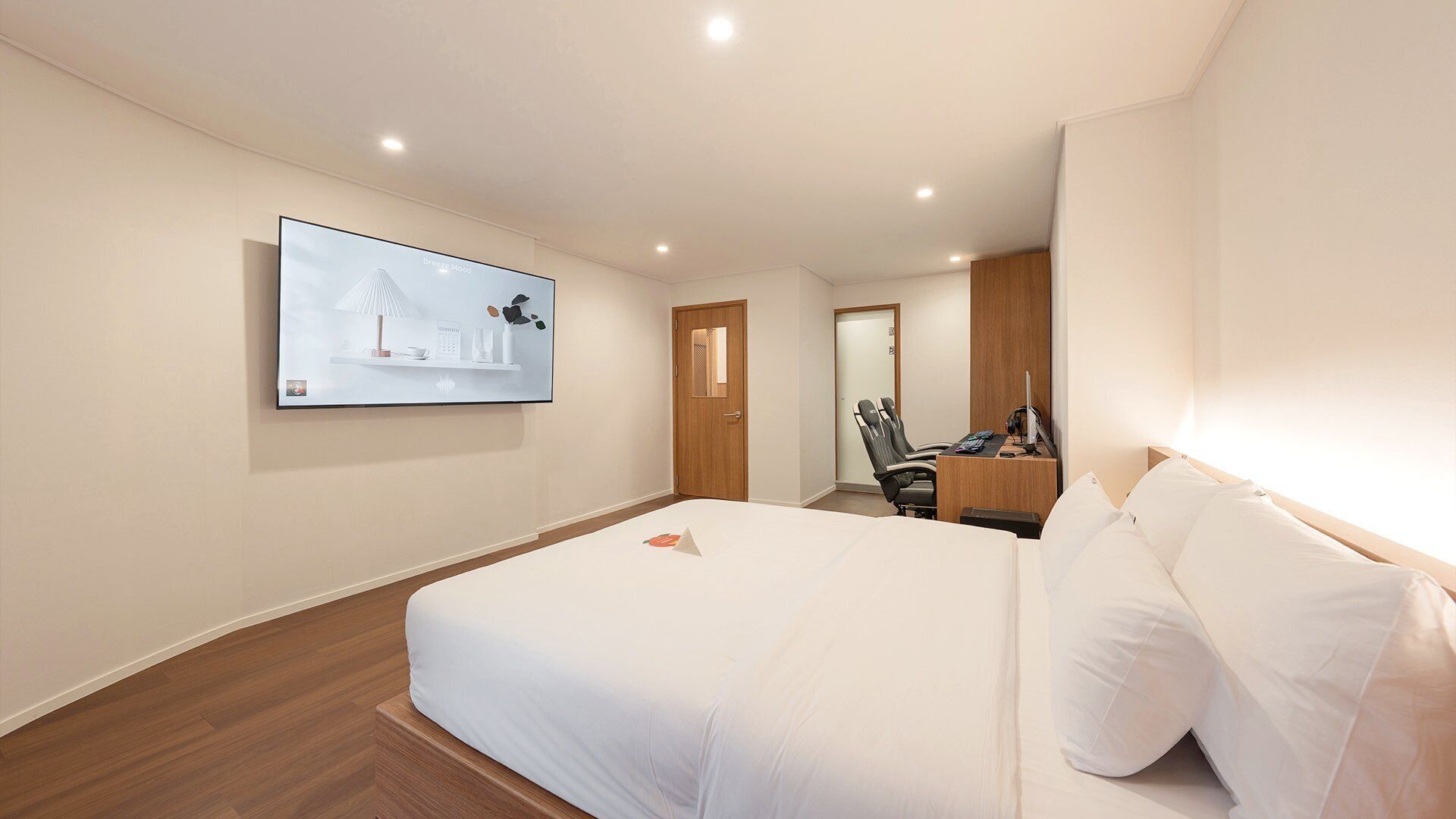 Habitación de hotel con una cama grande, un escritorio con computadora, una silla y un televisor instalado en la pared.