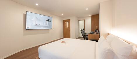 Habitación de hotel con una cama grande, un escritorio con computadora, una silla y un televisor instalado en la pared.