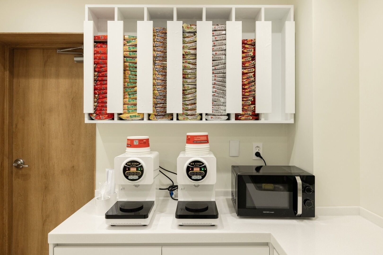 Una cocina con microondas, dos cocinas por inducción Ez Cook y un estante con alimentos envasados.