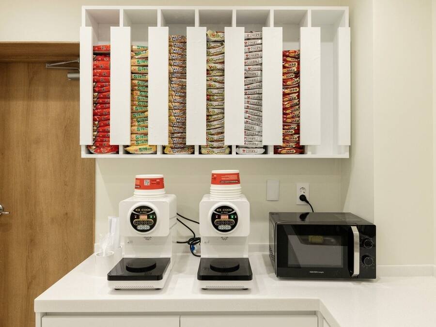 Una cocina con microondas, dos cocinas por inducción Ez Cook y un estante con alimentos envasados.