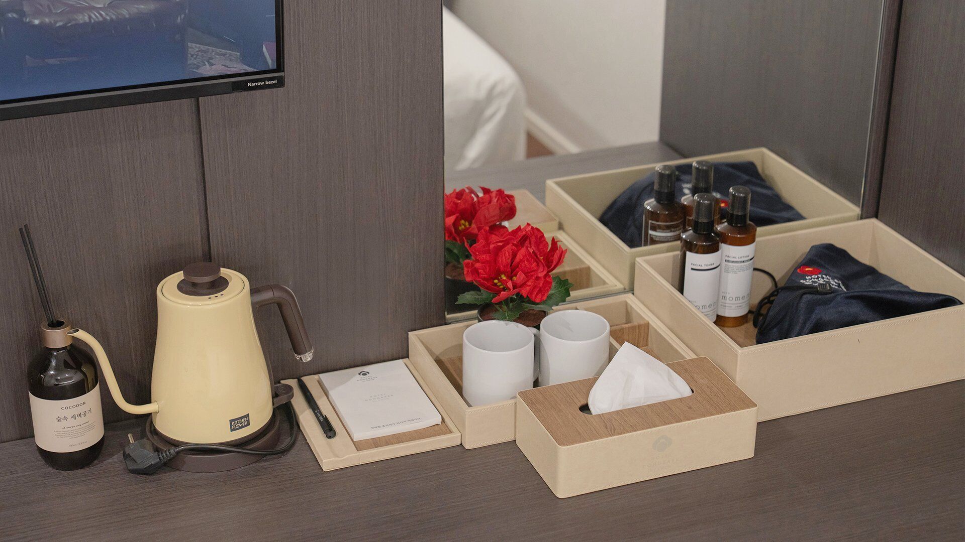 Una habitación de hotel con cama, televisor, cafetera, artículos de aseo y espejo.