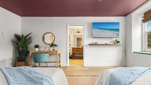 Ein Schlafzimmer mit zwei Betten, einem Schreibtisch, einem Stuhl, einer Zimmerpflanze, einem Spiegel und Blick auf den Strand.