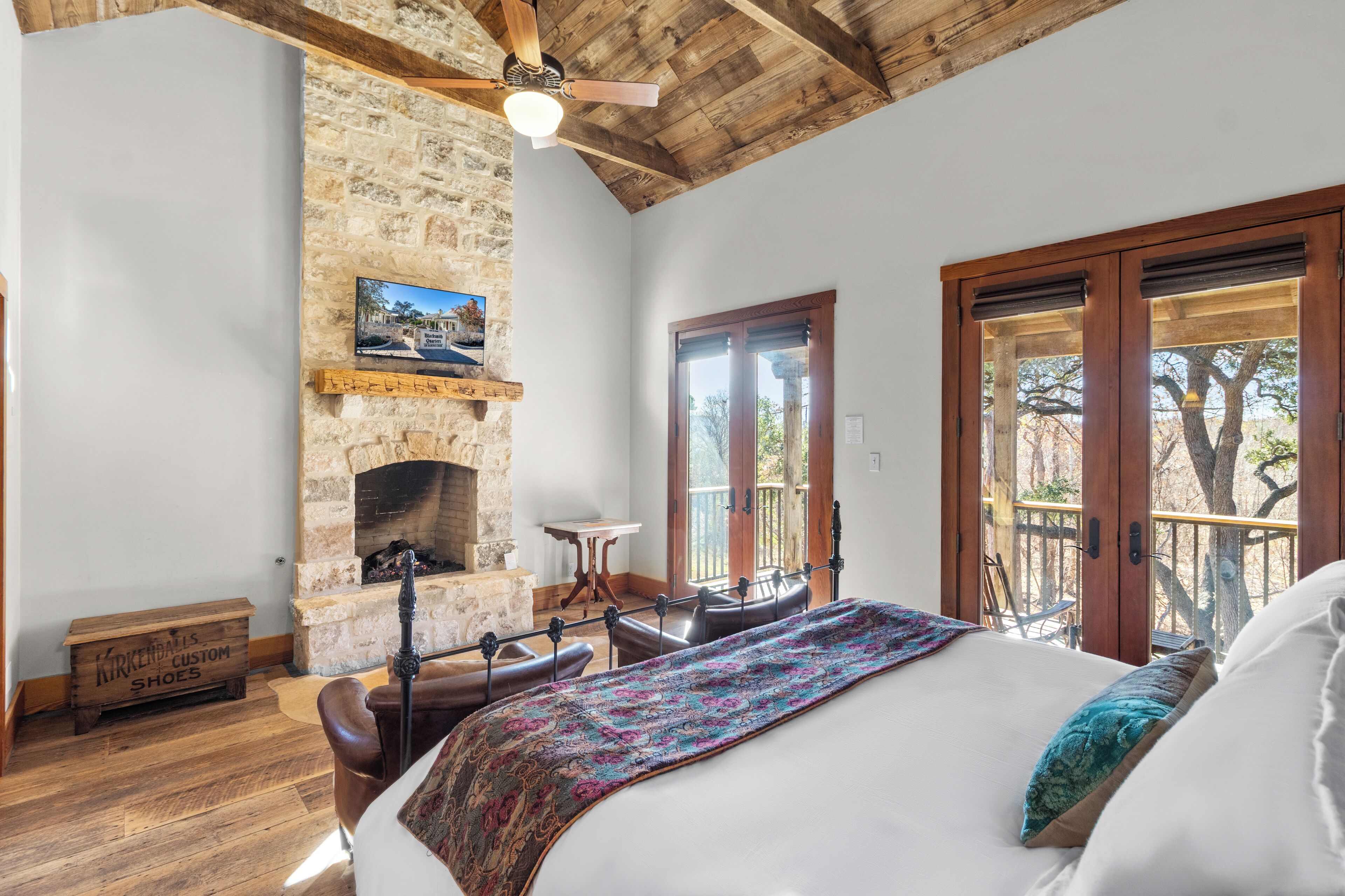 Una camera da letto con camino in pietra, soffitto in legno e un grande letto con coperta colorata.