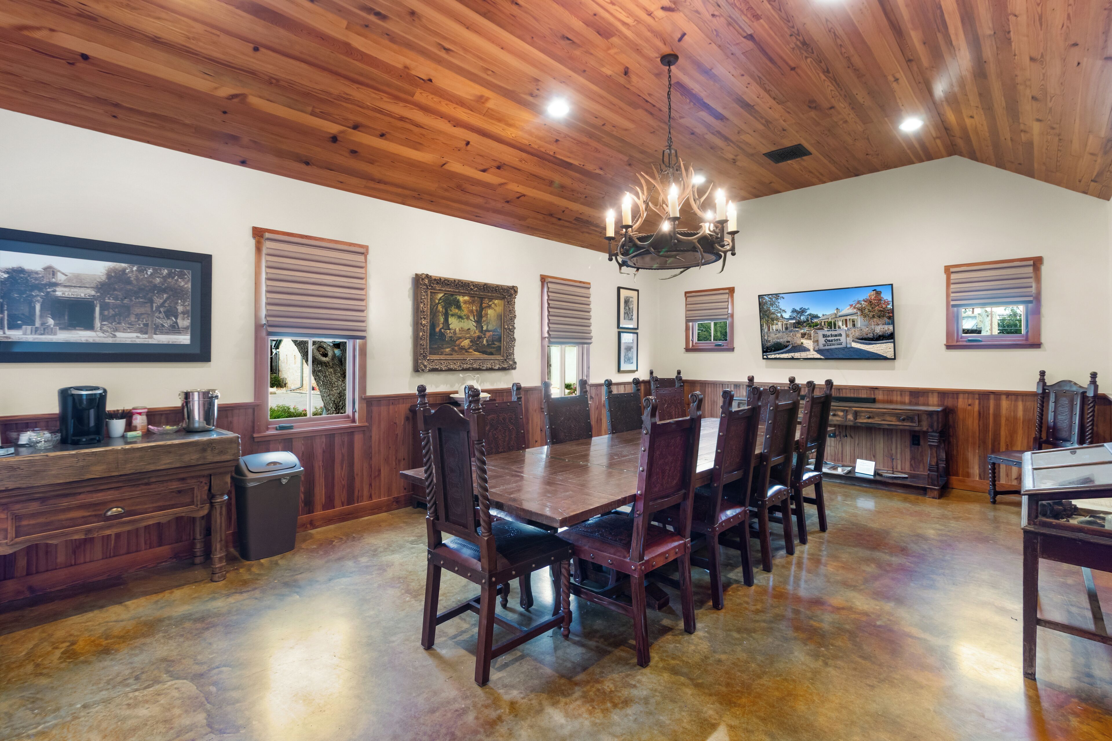 A dining area with a large wooden table and chairs, a chandelier, and framed pictures on the walls.