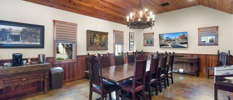 A dining area with a large wooden table and chairs, a chandelier, and framed pictures on the walls.